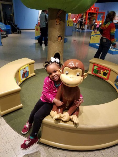 The author\'s daughter posing with Curious George at the Discovery Center Museum