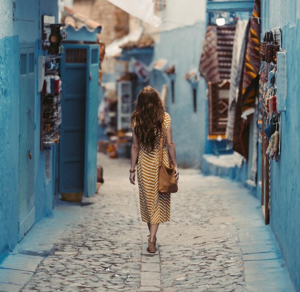 A woman walking through a narrow cobbled street with blue walls on the side.