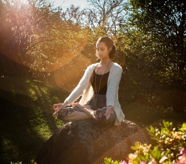 A woman sat on a rock meditating outside. 