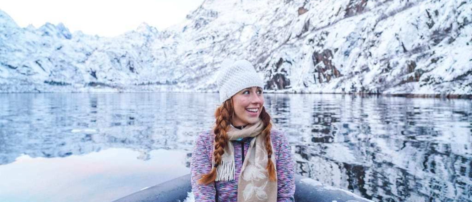 Valerie Joy Wilson sitting at the bow of a boat wearing a knitted hat with snow-covered hills behind her -- a presentation for Wanderful called "The myths and truths of being a solo female traveler"