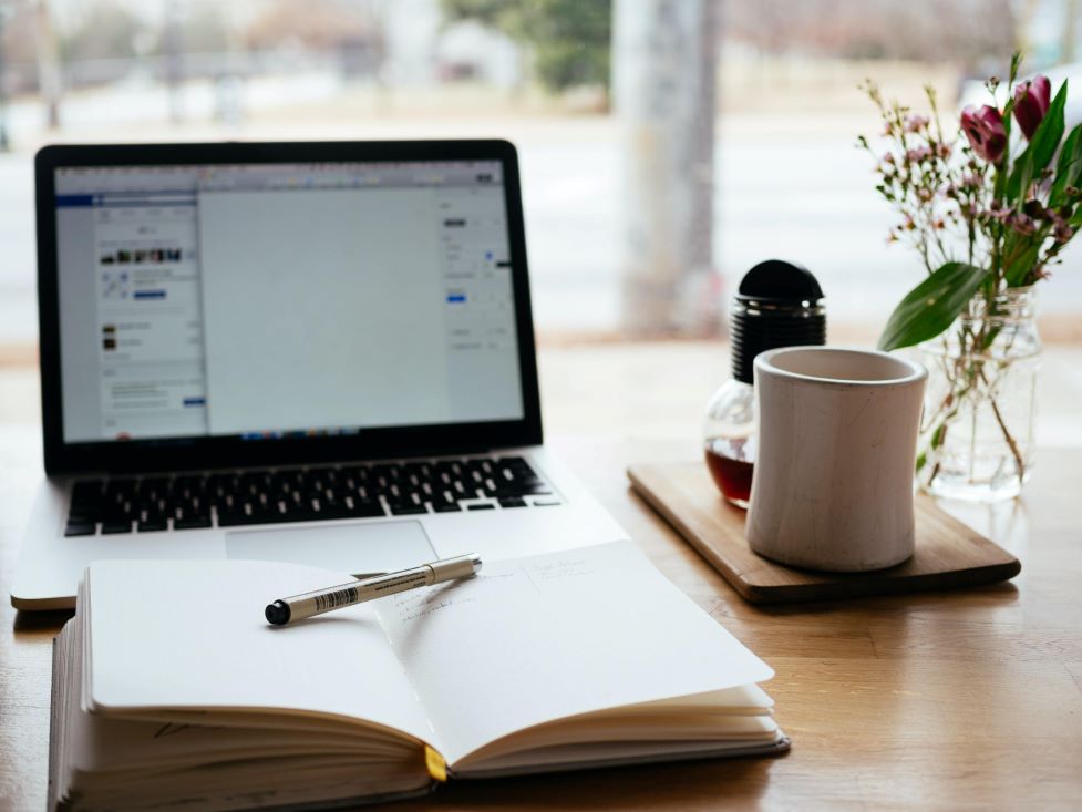 an open laptop and notebook with pen at the ready